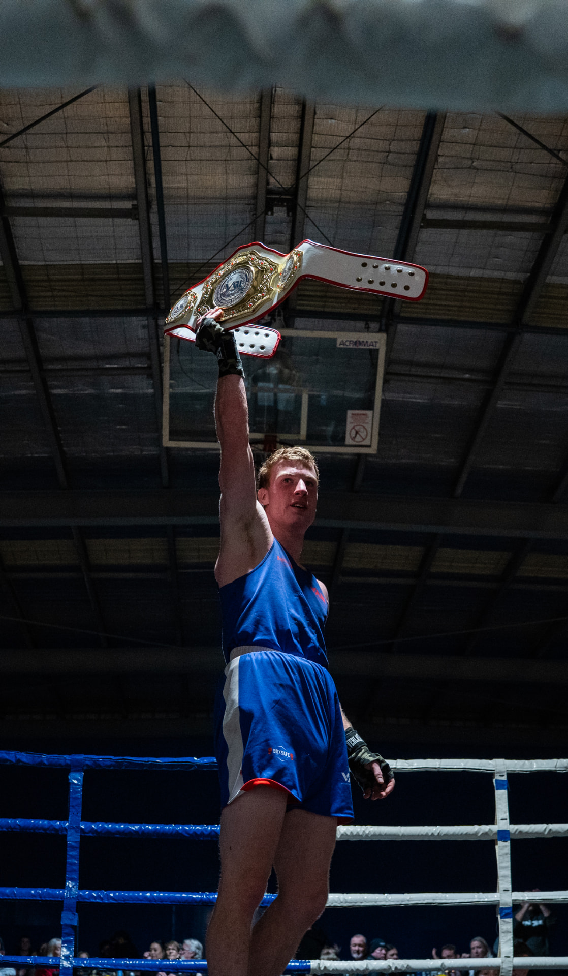 Victorious boxer raising a championship belt in the ring